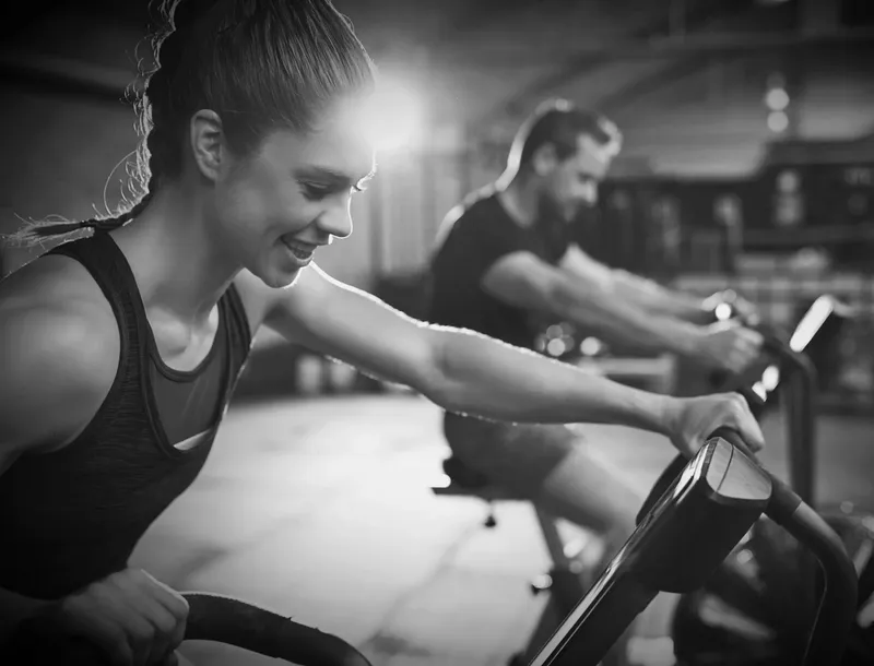 Couple using Rogue Assault Bikes in between strength exercises during private training at Forge