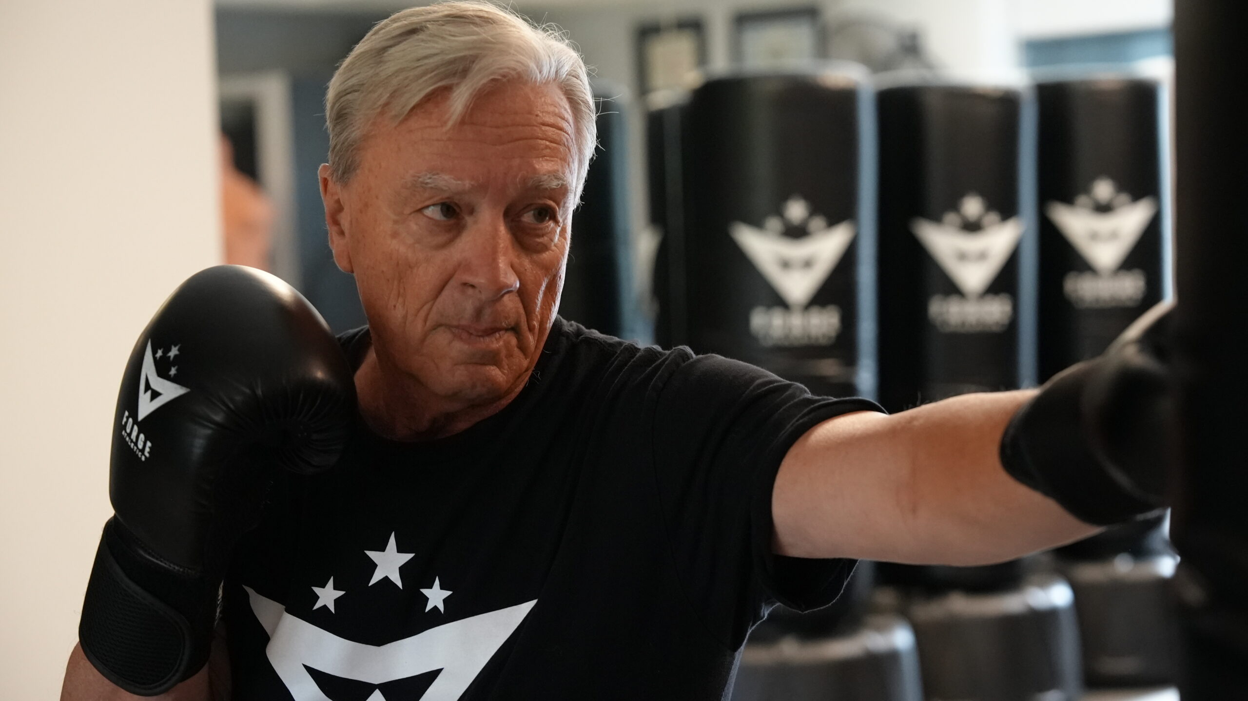 Senior man boxing a heavy bag with gloves at Forge Athletics Naples FL - coordination and strength training after 60