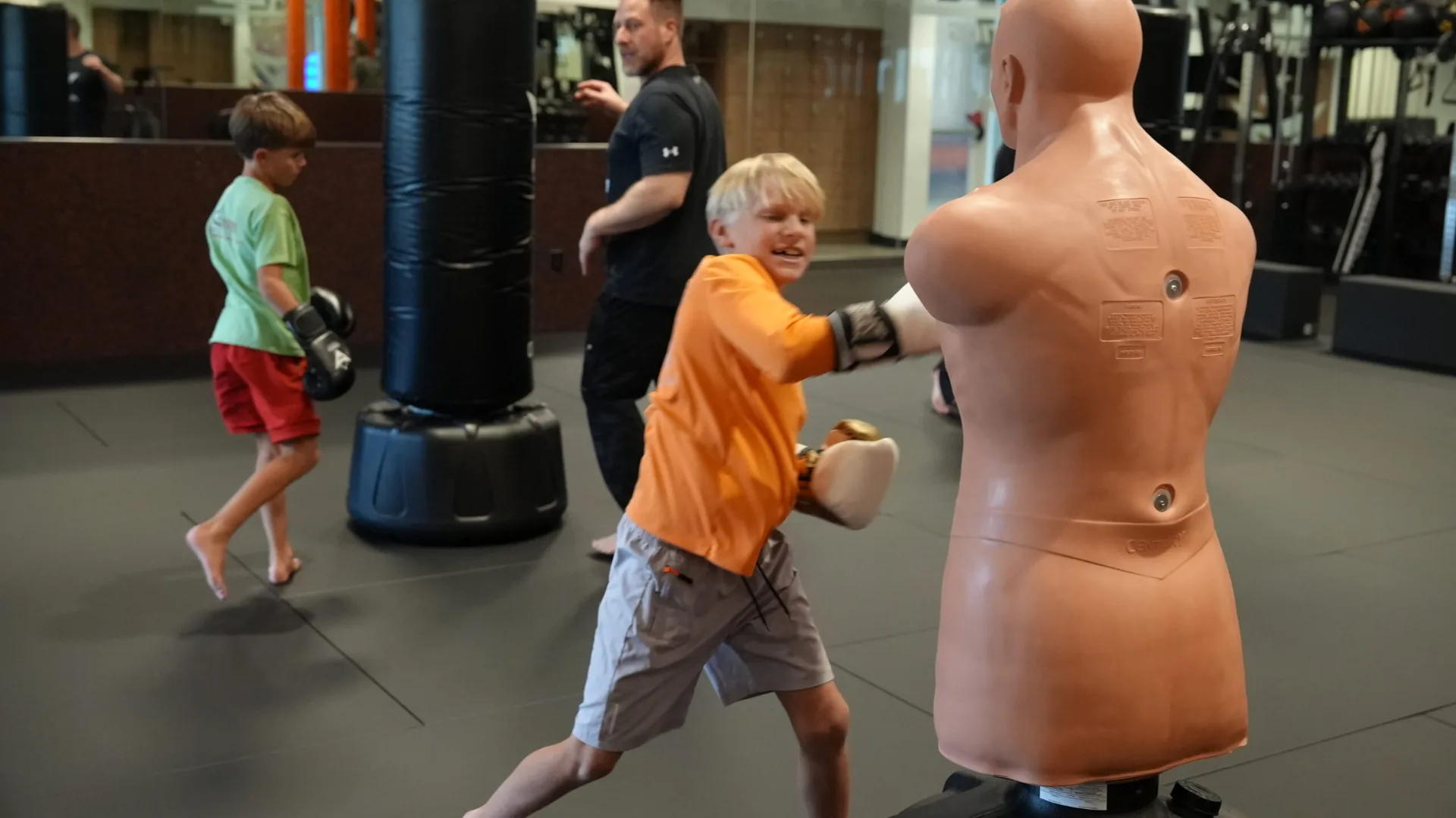 Young camper in an orange shirt punching a BOB training dummy at Forge Athletics themed summer camp in Naples FL